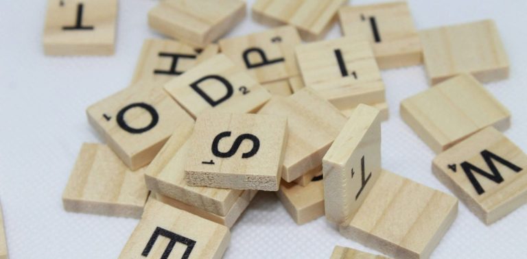 Erfolg in der Logopädie: wie das Wort aus Buchstaben, so setzt sich der Fortschritt aus kleinen Einheiten zusammen. Holzplättchen mit Buchstaben liegen ungeordnet auf dem Tisch
